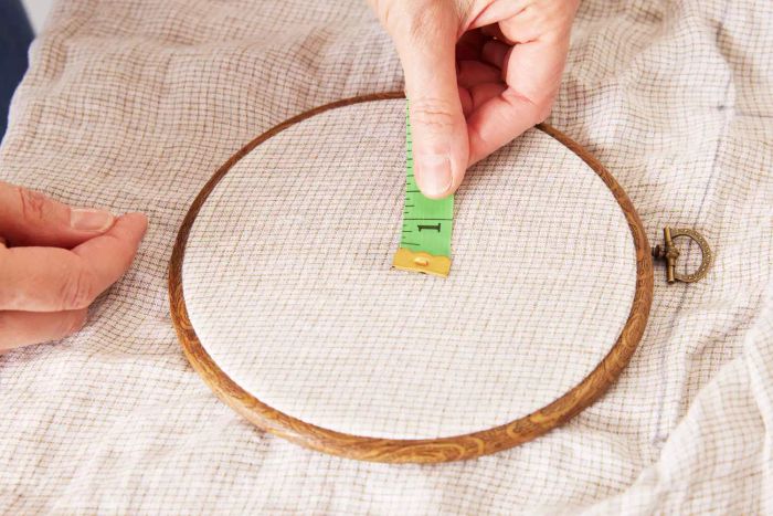 A person measuring the dimensions of the Crate & Barrel Garden Green Grid Natural Hemp Fiber Queen Bed Sheet Set.