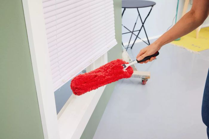 A person is dusting a windowsill with the OXO Good Grips Microfiber Hand Duster.