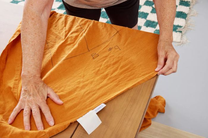 A person smoothing out a marked area of the Everly Hemp Sheet Set on a table