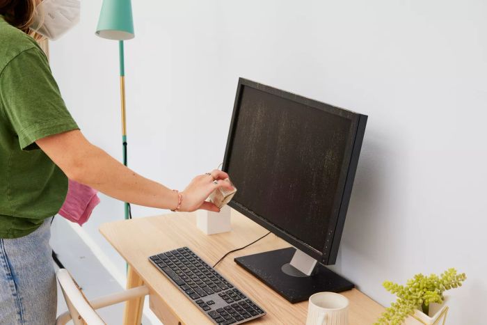 A person dusts a keyboard by sprinkling powder and then wipes it clean using the Amazon Basics Microfiber Cleaning Cloths.