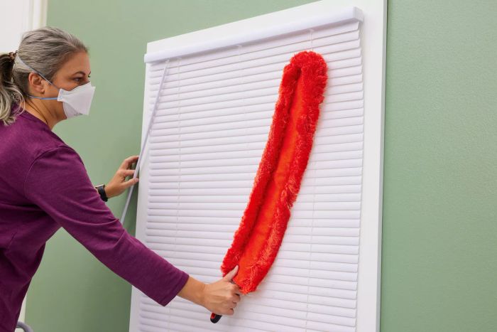 An individual uses the OXO Good Grips Under-Appliance Microfiber Duster to clean blinds.