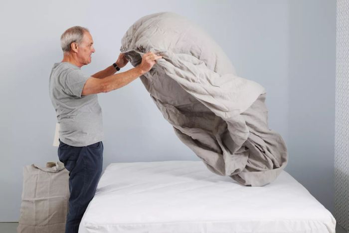 A person arranges the Delilah Home Hemp Sheet Set on a bed.