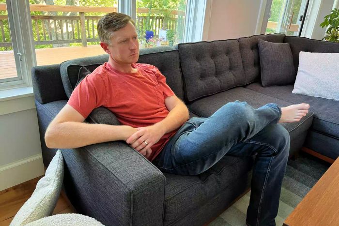 An individual seated on a gray Apt2B loveseat positioned by a window