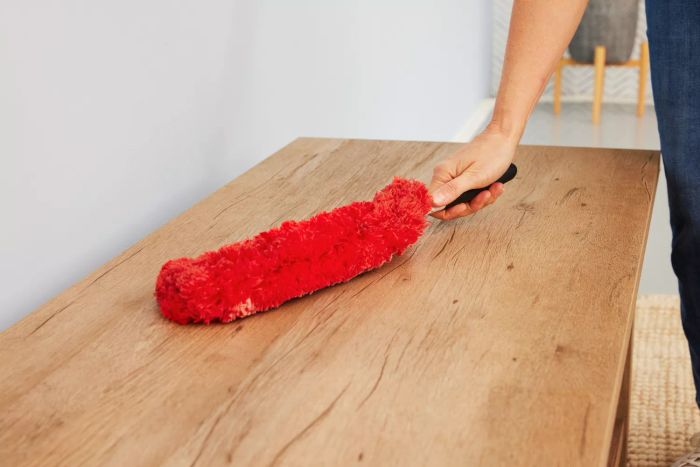 A person is dusting a surface with the OXO Good Grips Microfiber Hand Duster.