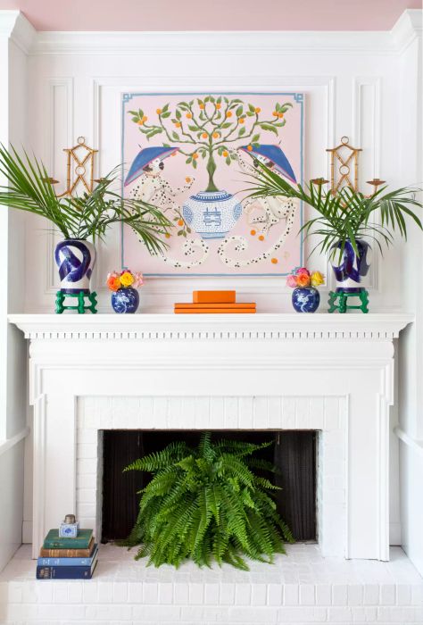 A stylish mantel featuring pink artwork and ferns surrounding a white fireplace.