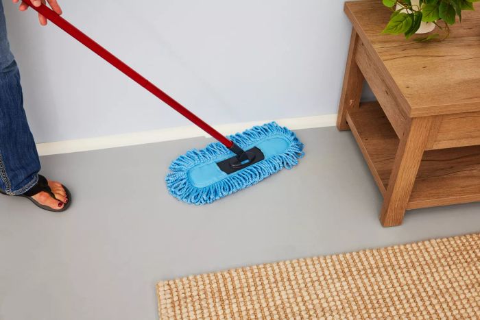 A person is dusting under a table with the O-Cedar Dual-Action Microfiber Sweeper Dust Mop.