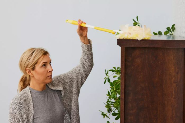 A person is dusting using the Swiffer 360 Heavy Duty Duster with Extendable Handle Starter Kit.