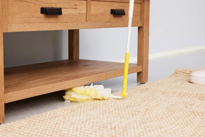 A person is using the Swiffer 360 Duster to clean beneath a table.