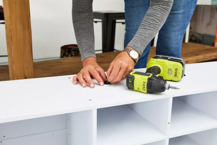 A person assembling the VASAGLE Shoe Bench using screws and a drill machine