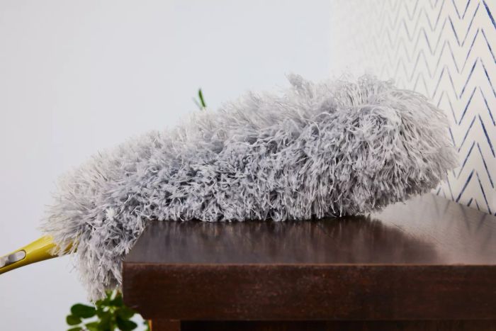 The DocaPole Microfiber Duster with Extension Pole is used to clean a shelf.
