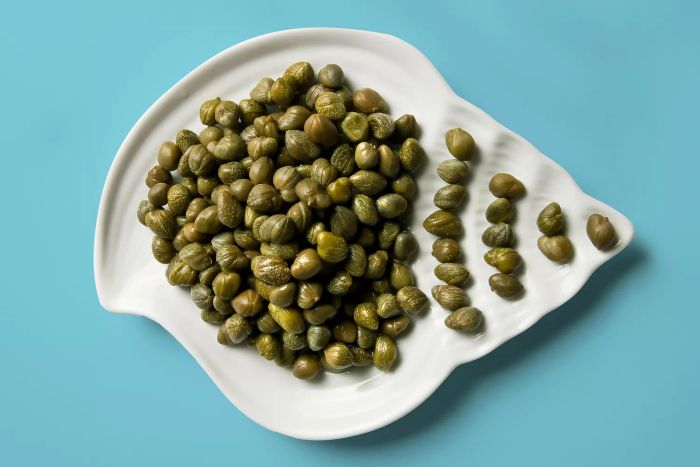 Capers arranged in a shell-shaped dish set against a blue background.