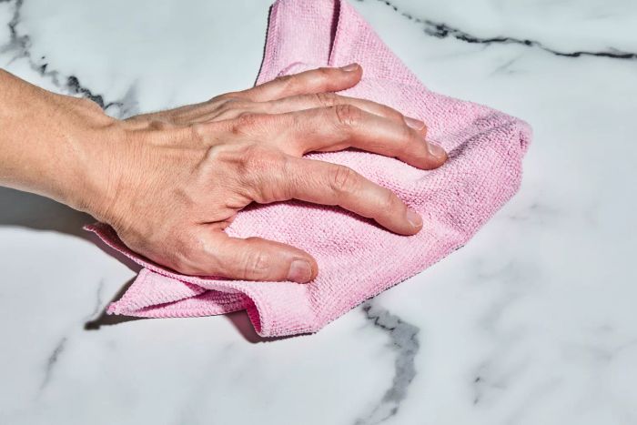 A person uses the Amazon Basics Microfiber Cleaning Cloth to wipe down a white marble tabletop.