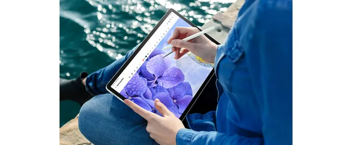  Một người ngồi gần nước đang cầm Galaxy Tab S9 FE+ ở chế độ Phong cảnh và sử dụng S Pen để vẽ hình bông hoa trong ứng dụng Samsung Notes mở trên màn hình.